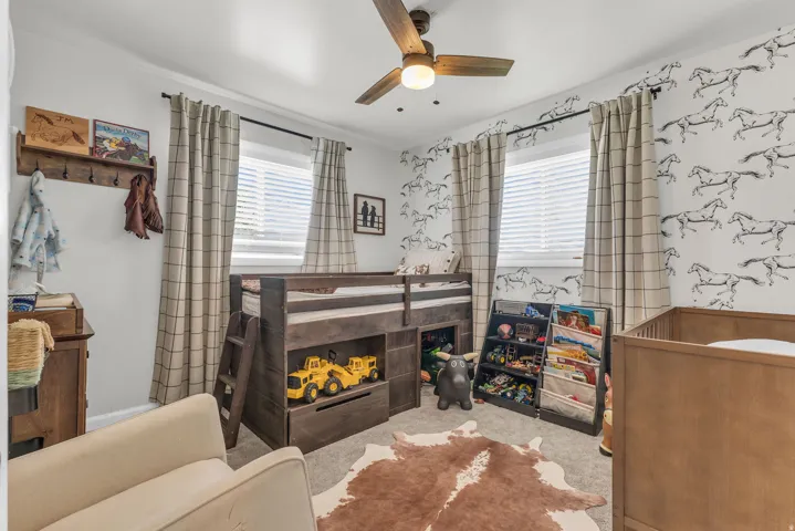 Room featuring light gray walls, two windows with white blinds and plaid drapes, and a wood-finish ceiling fan with lighting
