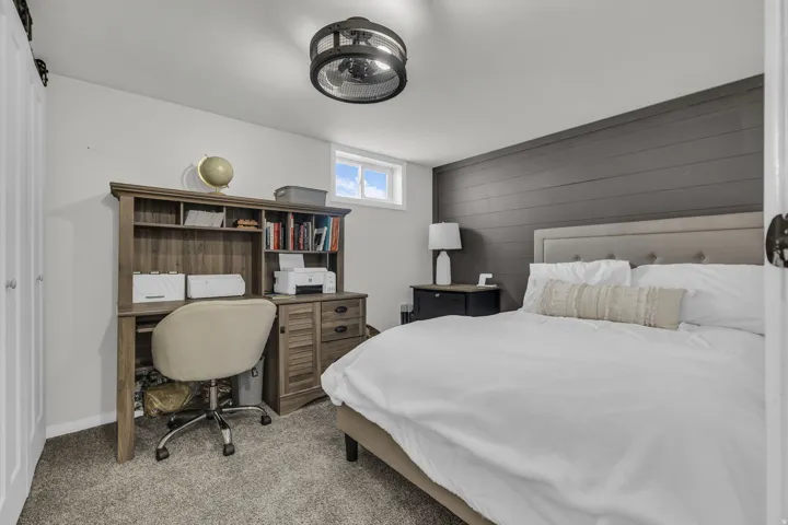 Carpeted room featuring a dark shiplap accent wall, light gray painted walls, a built-in wood-finish desk with shelving, and a window providing natural light