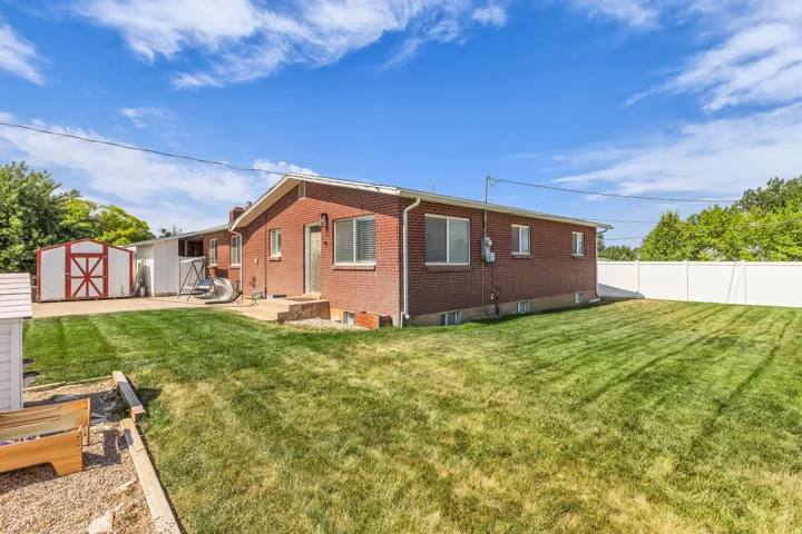 Expansive rear yard featuring a large lawn area, a white vinyl privacy fence, and a brick exterior with white-framed windows
