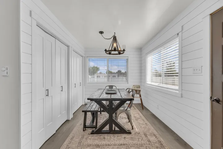 Dining area featuring shiplap walls, wood-finish flooring, two windows with blinds, and built-in closet storage with bi-fold doors