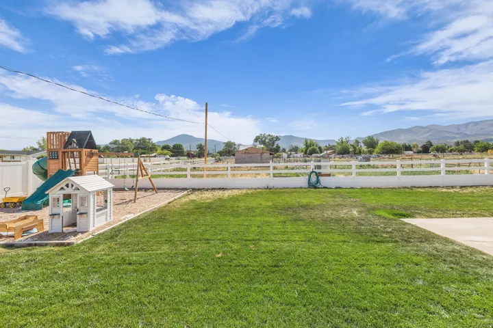 Expansive backyard featuring a green lawn, white fencing, and a distinct play area with a wooden playset and swing set