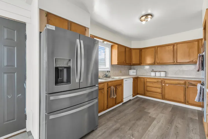 Kitchen featuring wood-finish cabinetry, stainless steel refrigerator, white dishwasher, light-colored countertops, and wood-finish flooring