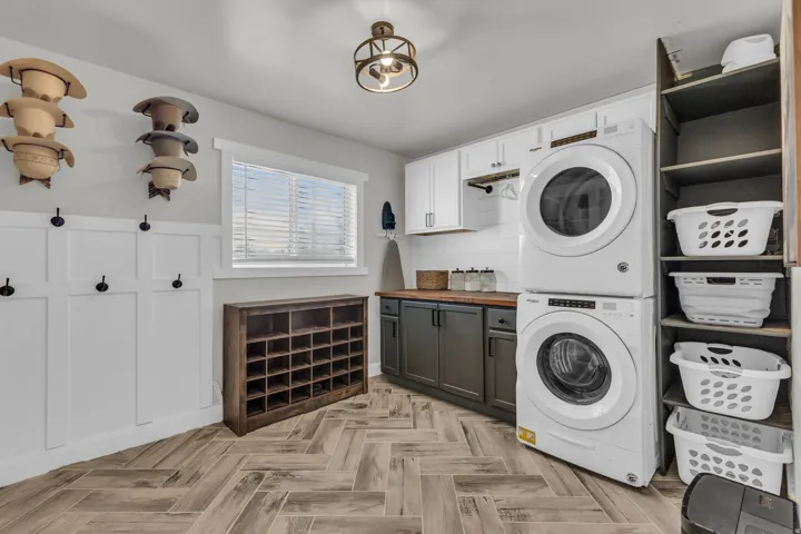 Laundry room featuring herringbone wood-finish flooring, white board and batten paneling with integrated hooks, a window with blinds, and a built-in shelving unit
