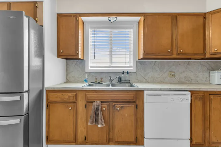 Kitchen featuring wood cabinetry, a double basin stainless steel sink, and a white dishwasher