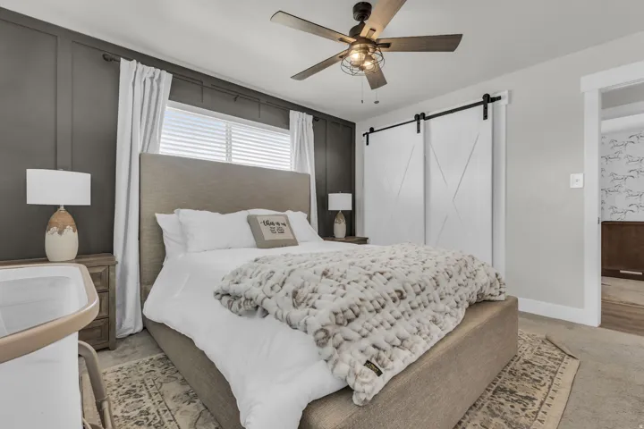Bedroom featuring panel accent wall, window with blinds, dual barn doors, and ceiling fan with integrated lighting