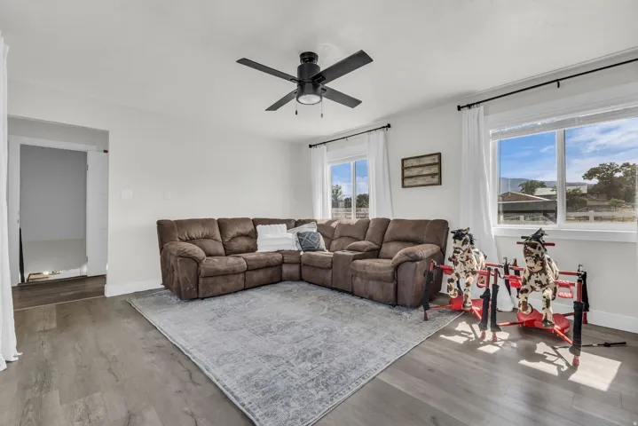 Spacious room featuring wood-finish flooring, a ceiling fan with integrated lighting, and multiple windows
