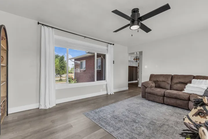 Spacious room featuring wood-finish flooring, a large picture window, and a ceiling fan with integrated lighting