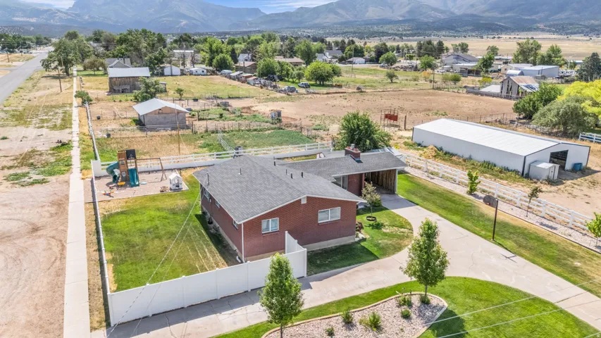 Red brick ranch-style residence featuring a gray shingle roof, a large concrete driveway, and a white privacy fence