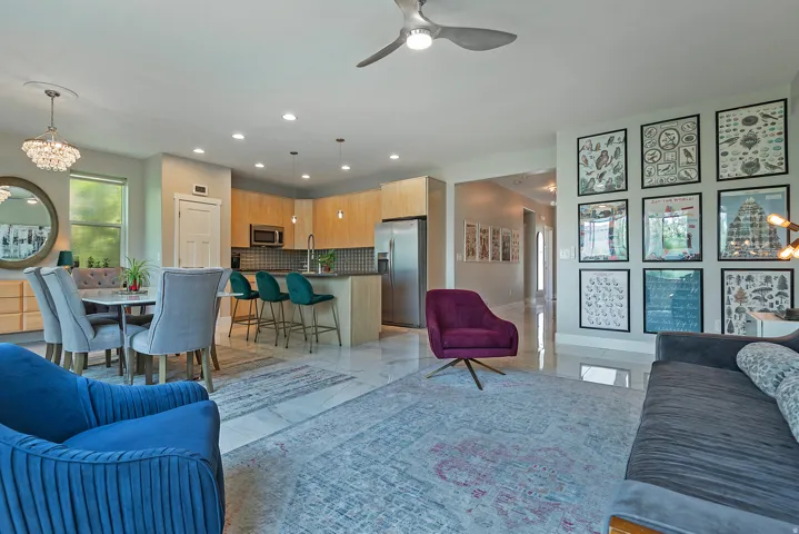 Open-concept living space featuring wood-finish cabinetry, stainless steel appliances, a kitchen island with a breakfast bar, recessed lighting, and large format tile flooring