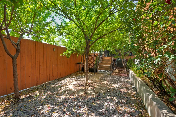 Gravel patio area featuring mature trees, a wooden privacy fence, and concrete retaining walls
