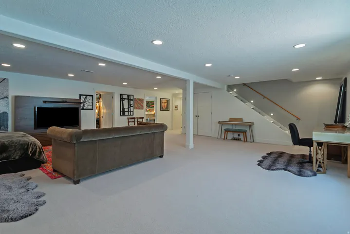 Spacious lower-level area featuring recessed lighting, light-toned carpeting, a built-in entertainment center with integrated shelving, a staircase with a wood handrail and integrated lighting, and a double-door closet