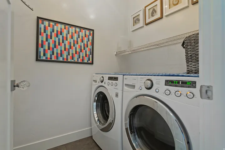 Dedicated laundry area featuring a front-loading washer and dryer, a wire shelving unit, and white walls with baseboard trim
