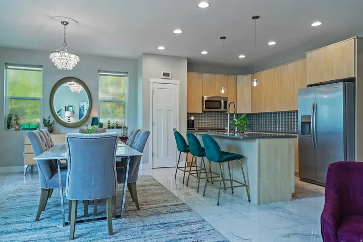 Open-concept kitchen and dining area featuring light wood-finish cabinetry, stainless steel appliances, and a dark countertop island with pendant lighting