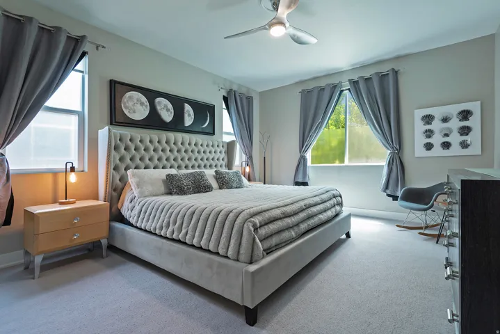 Spacious room featuring light gray wall paint, two windows with gray curtains, and a ceiling fan