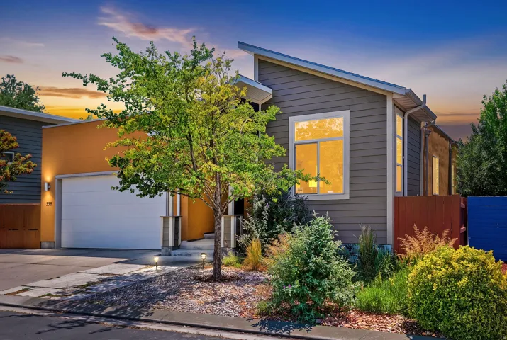 Contemporary exterior featuring multi-toned siding, an attached garage, and a mature tree