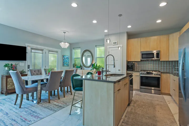 Open-concept kitchen and dining area featuring light wood-finish cabinetry, stainless steel appliances, a center island with sink, recessed lighting, and double glass-paneled doors