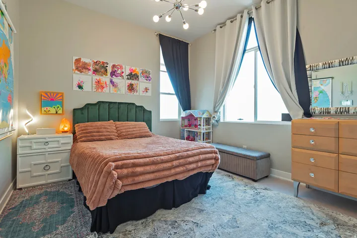 Room featuring a large window with floor-length drapes, a green upholstered headboard, and light-toned walls