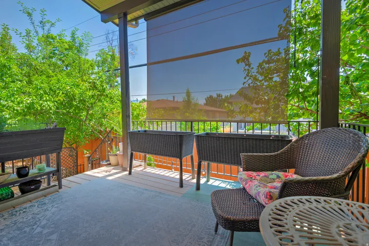 Covered patio area featuring a light-toned deck, dark support beams, and a dark privacy screen