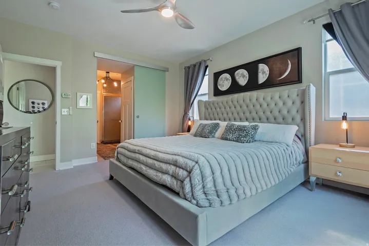 Carpeted bedroom featuring a large tufted headboard, two windows with curtain rods, and a ceiling fan with integrated lighting