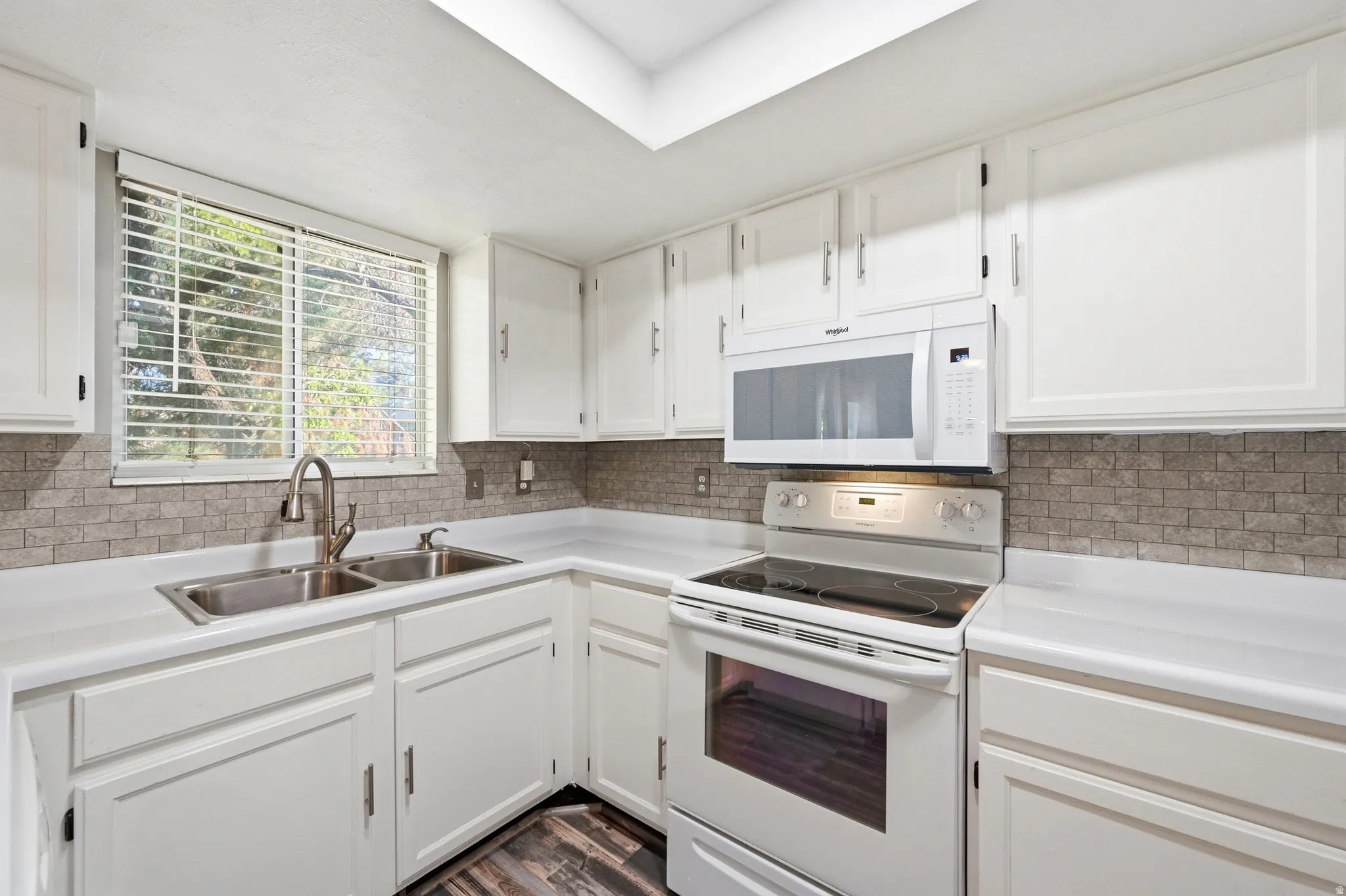 White cabinetry, white countertops, stainless steel double basin sink, white range, and stone tile backsplash