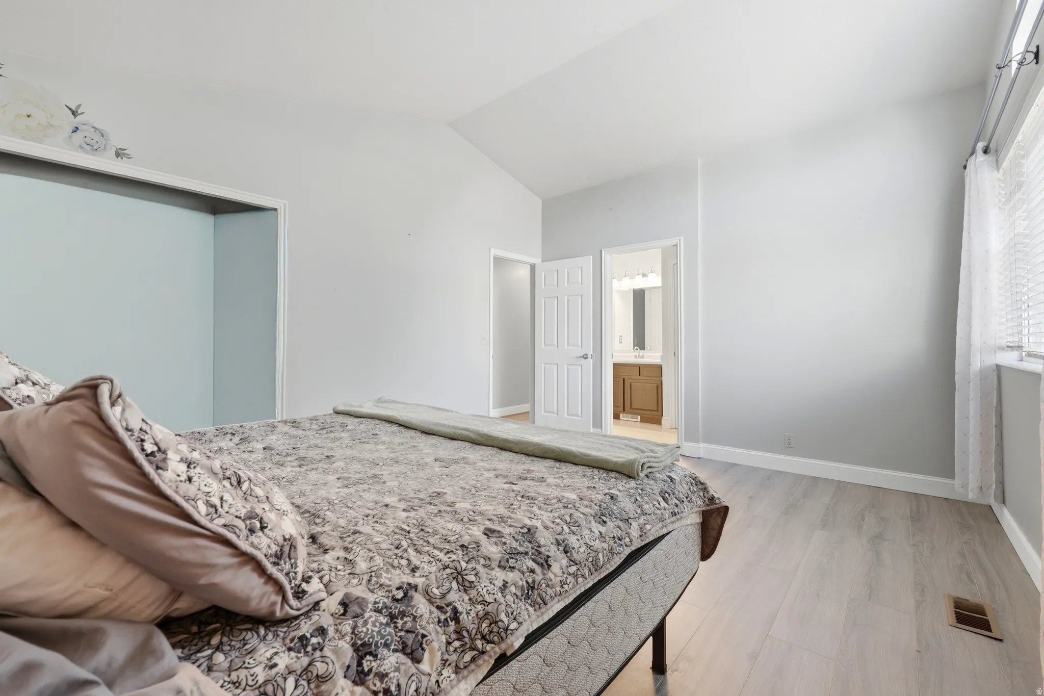 Vaulted ceilings accent this spacious room featuring light wood-finish flooring, a window with horizontal blinds, and a built-in closet space