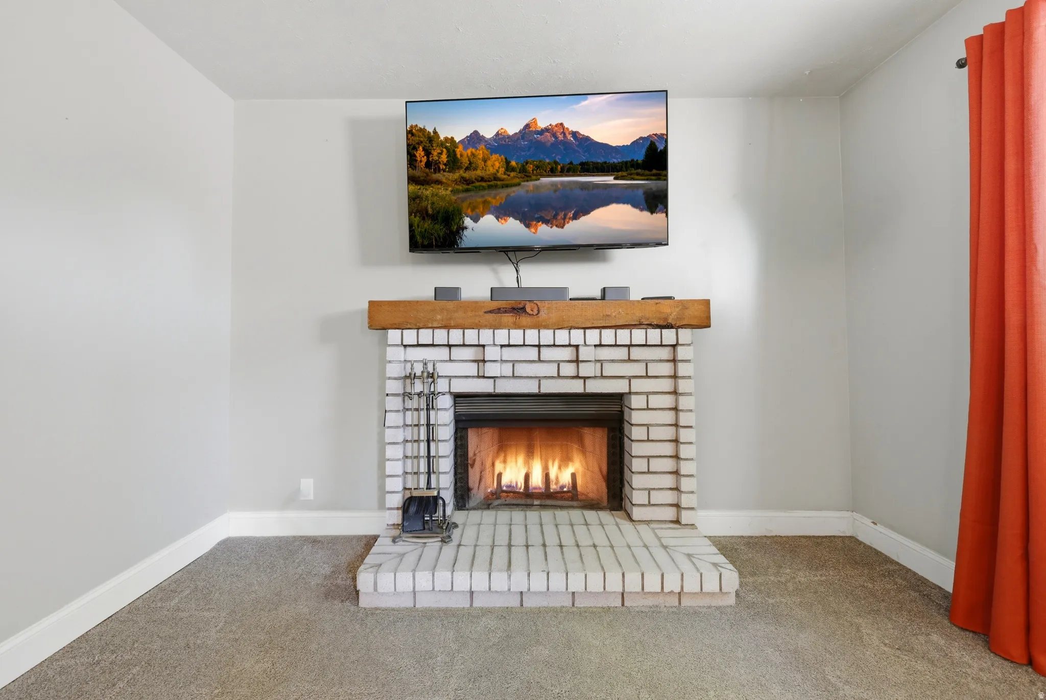 Brick fireplace with a wood mantle, complemented by light gray walls and carpet flooring
