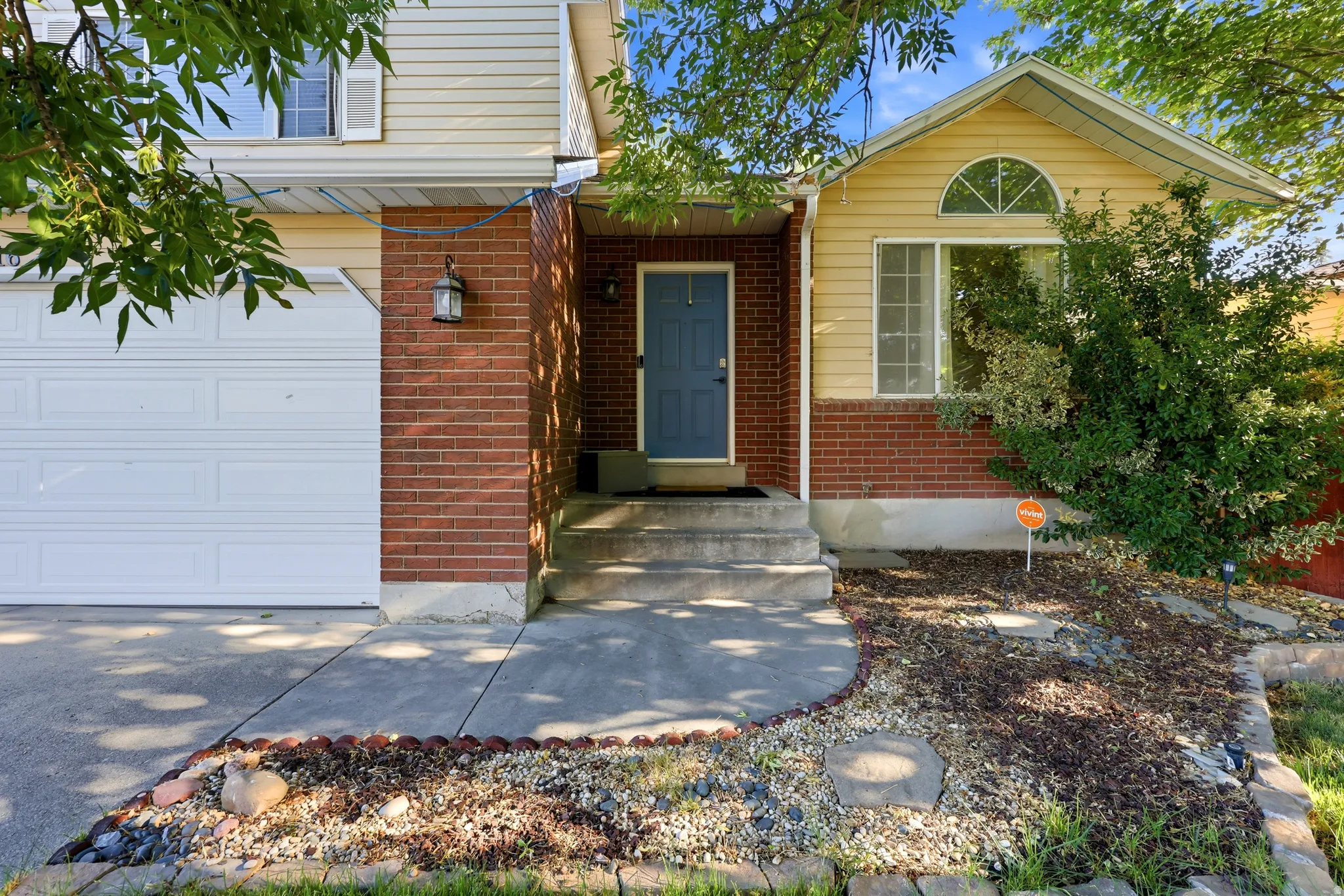 Brick and siding exterior with an attached garage, concrete walkway, and landscaped front garden