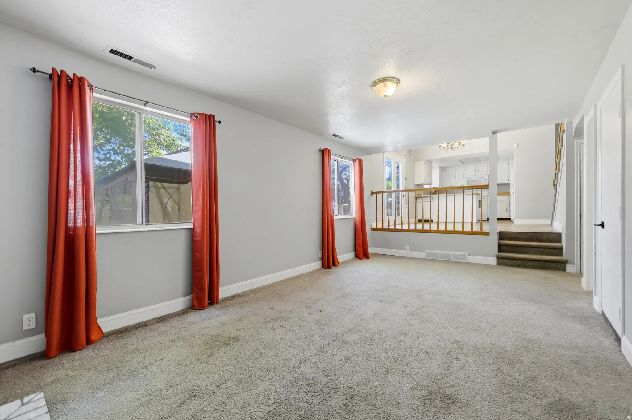 Spacious living area featuring light gray walls, carpet flooring, and two windows