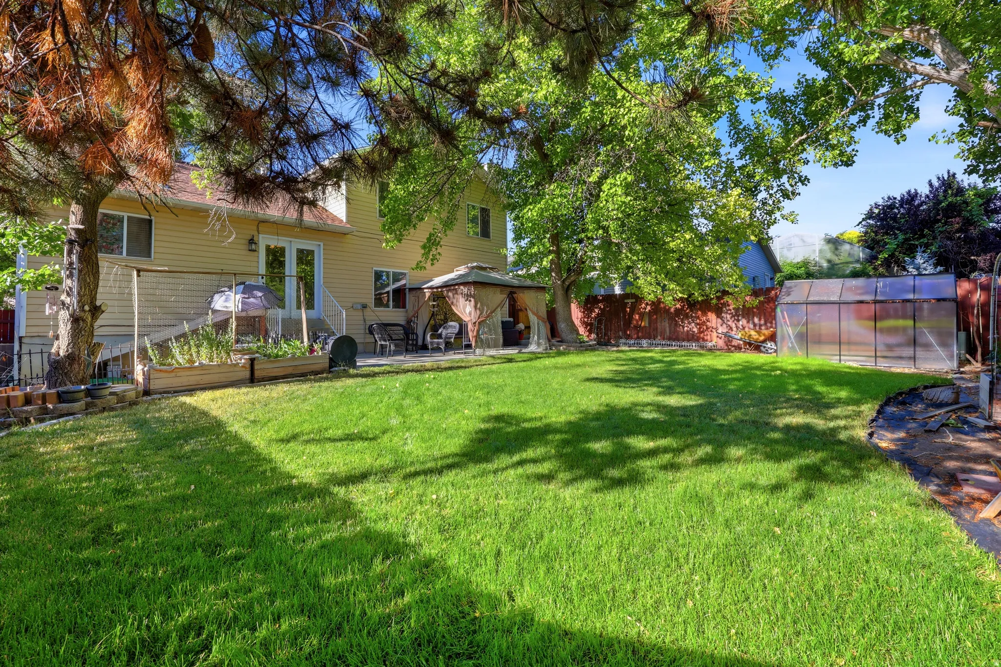 Expansive green lawn with mature trees and a greenhouse structure