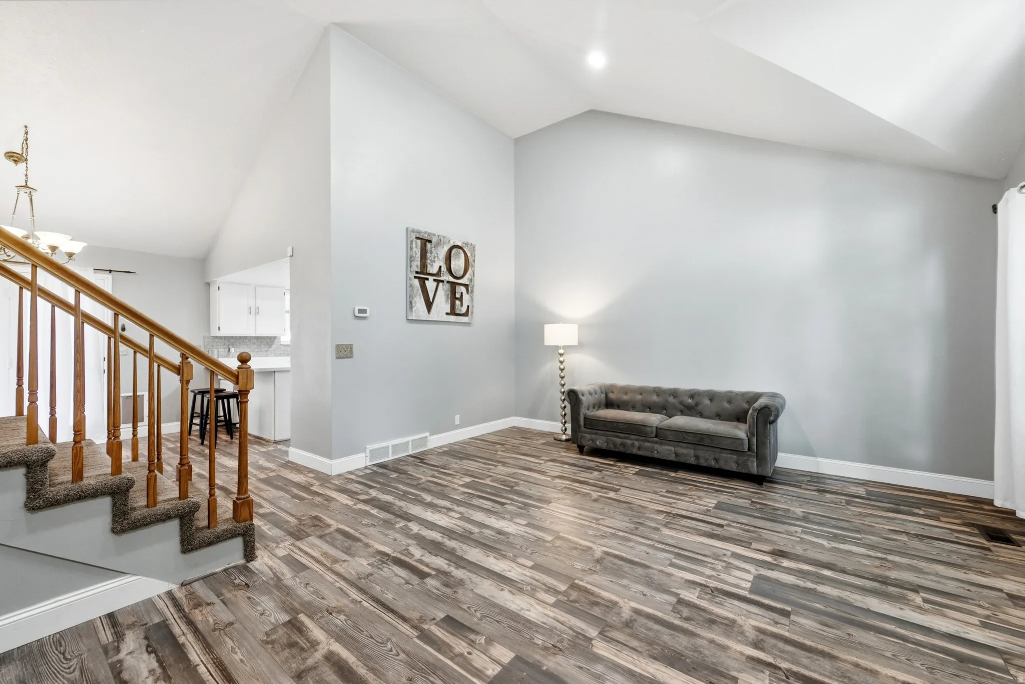 Vaulted ceilings, wood-finish flooring, staircase with wood railing, white baseboards, and neutral wall tones