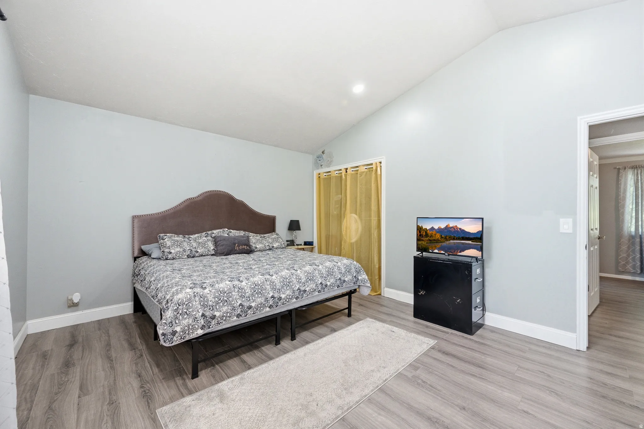 Vaulted ceiling, wood-finish flooring, light gray wall color, recessed lighting, and a closet with a curtain enclosure
