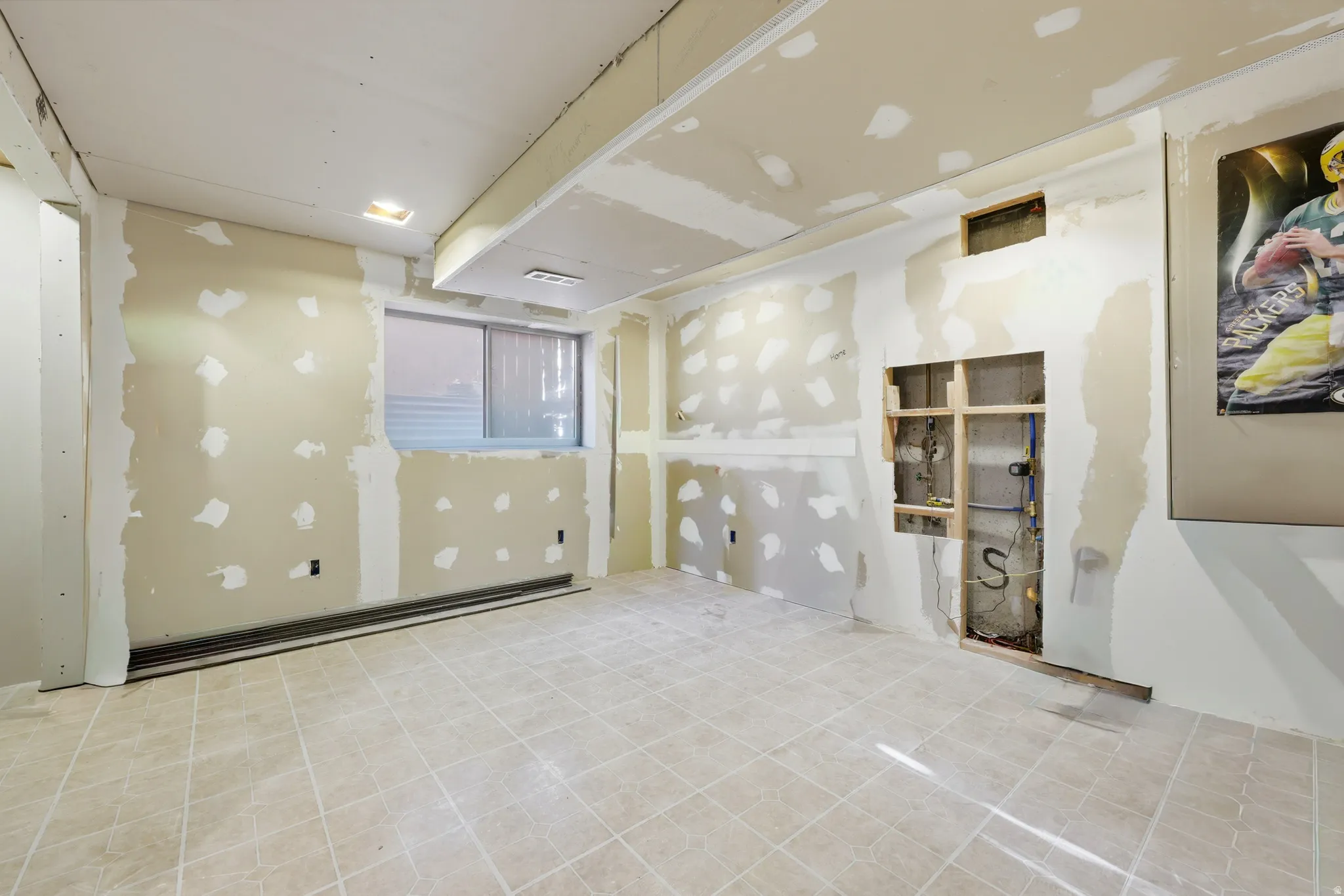 Spacious room featuring neutral tile flooring, a window, recessed lighting, and exposed framing for a custom built-in