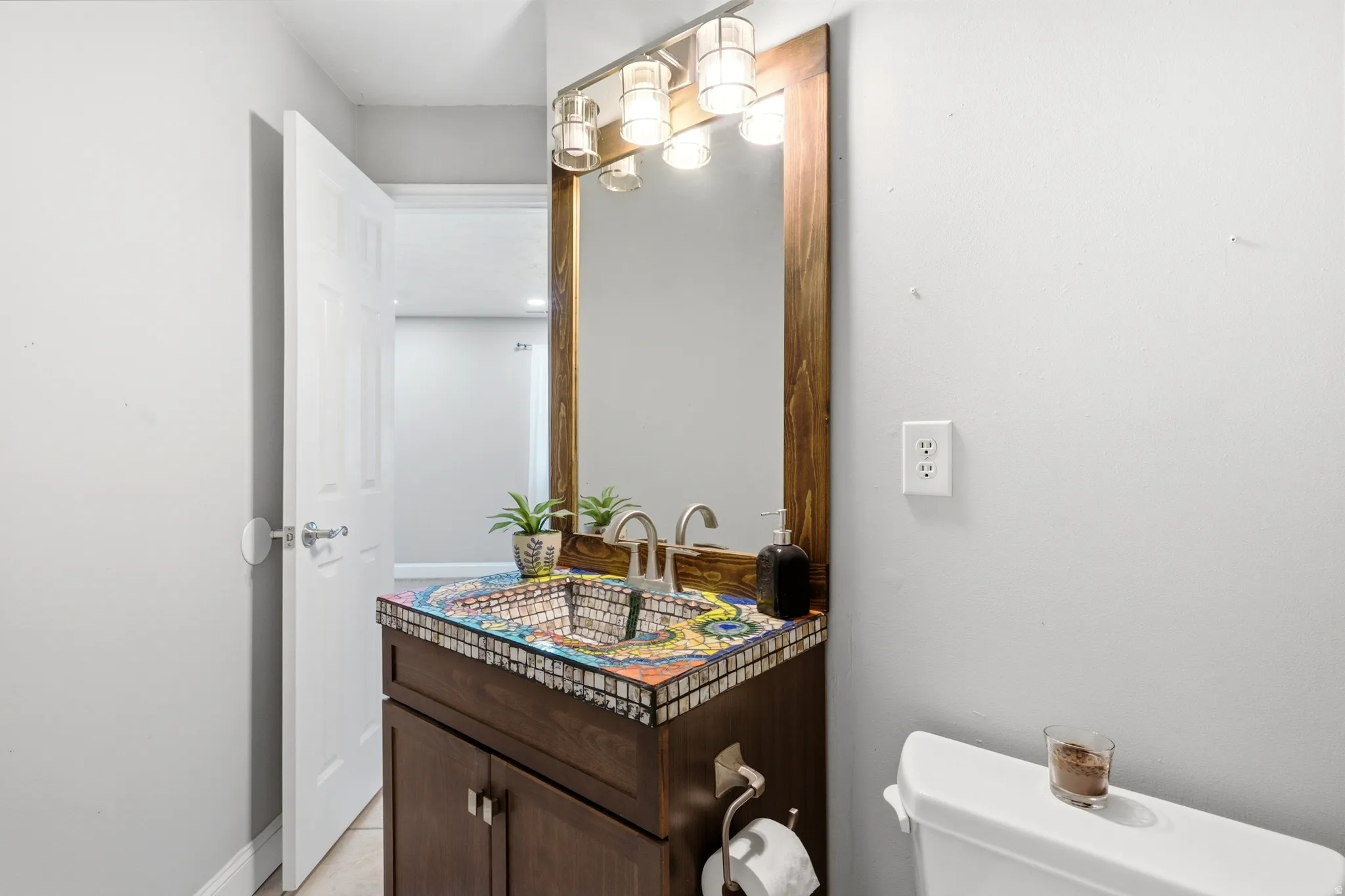 Vanity featuring a unique mosaic countertop, integrated basin, and a wood-framed mirror
