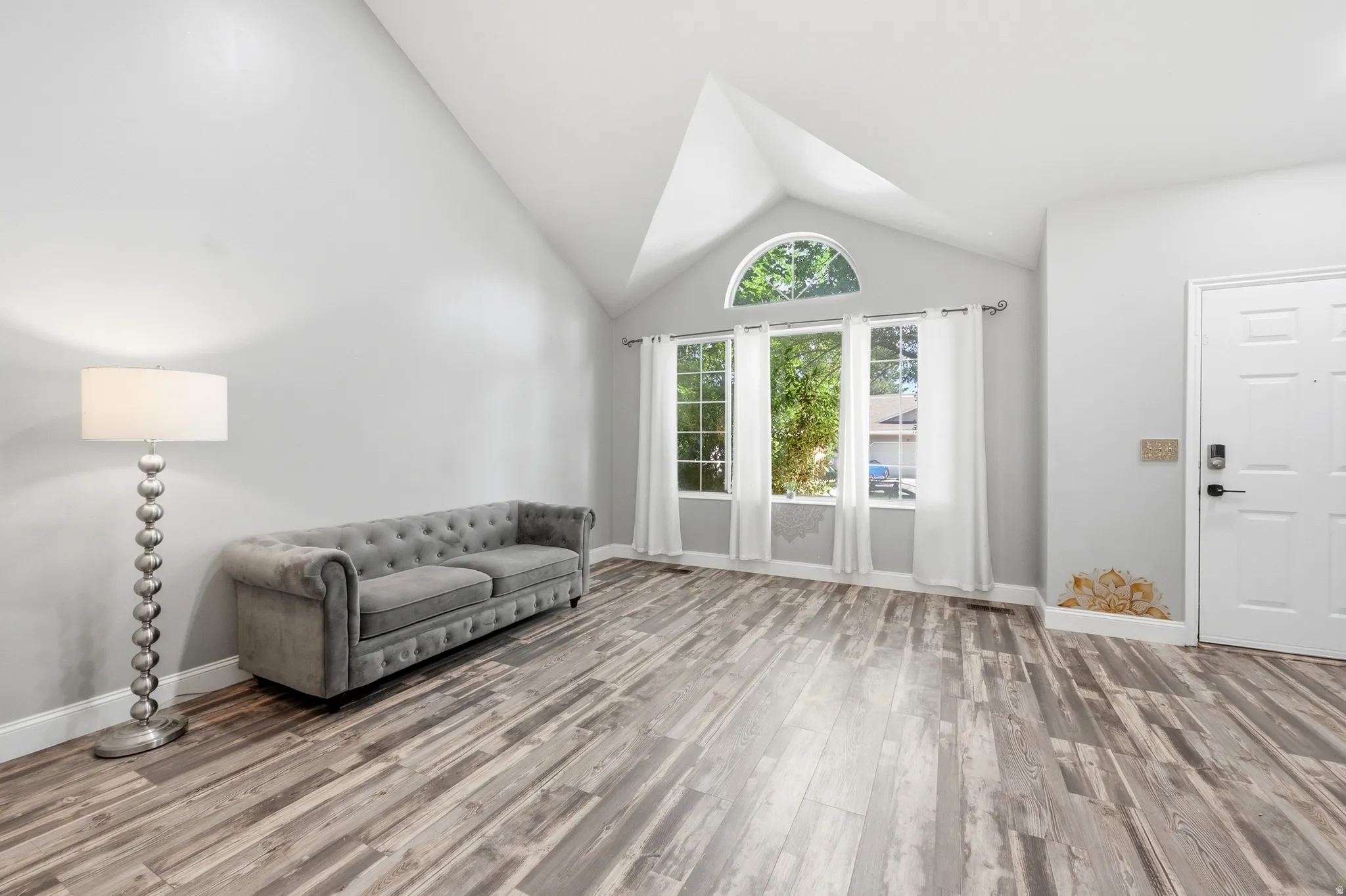 Vaulted ceiling, wood-finish flooring, white walls, multiple windows, and a white entry door