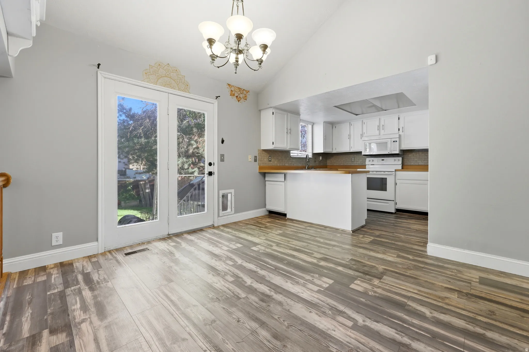 Vaulted ceilings enhance this open-concept space featuring wood-finish flooring, a contemporary chandelier, and French doors leading outdoors