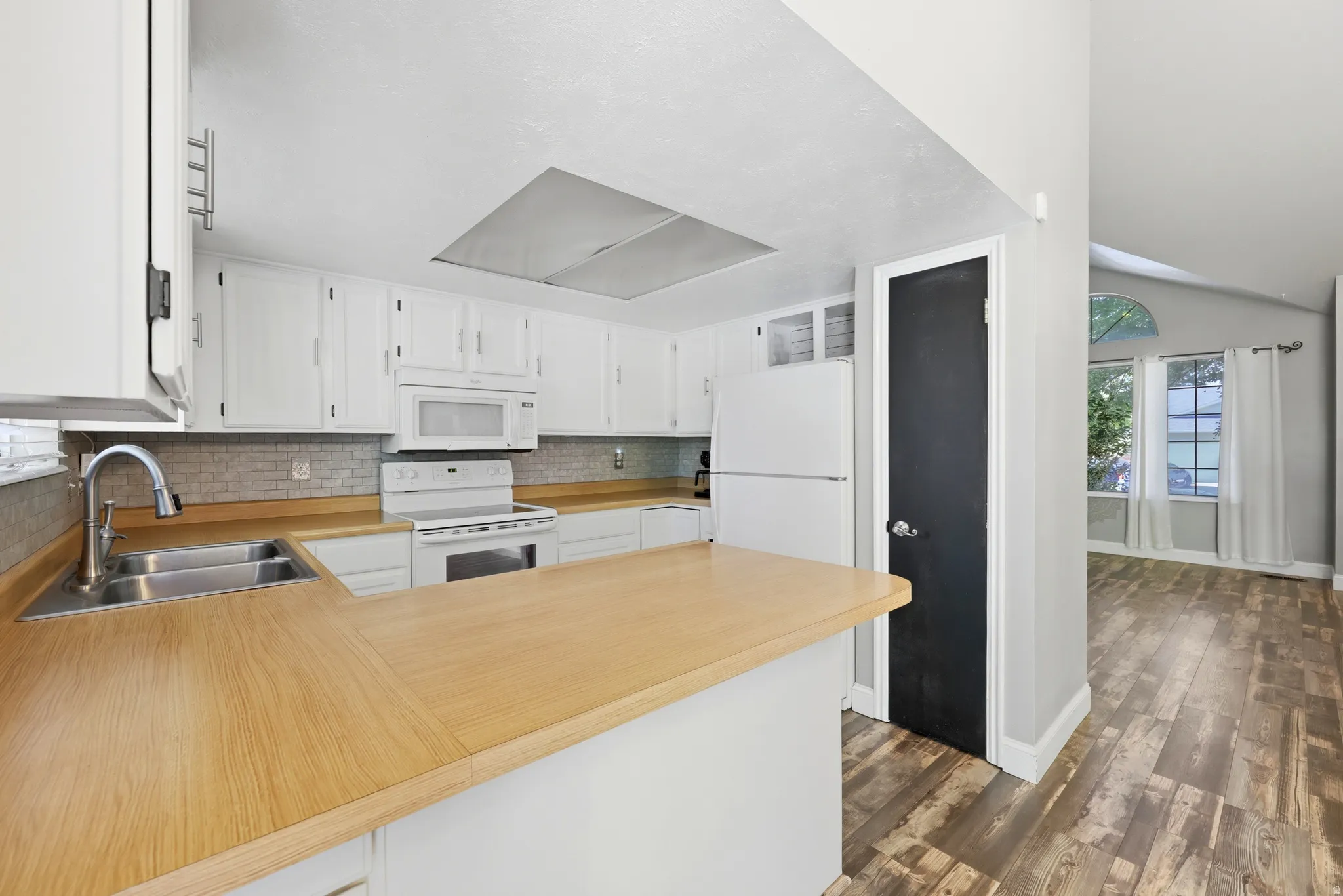 Open-concept kitchen featuring white cabinetry, light wood-finish countertops, and a stainless steel double-basin sink with a gooseneck faucet