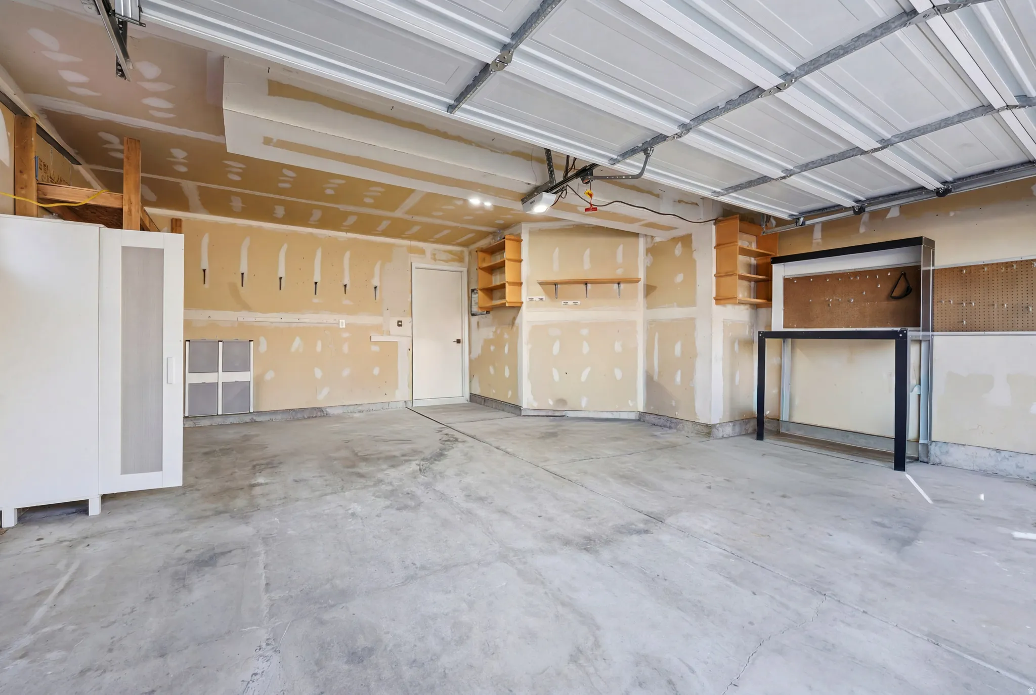 Spacious garage featuring a concrete floor, overhead garage door, built-in shelving, and a workstation with pegboard
