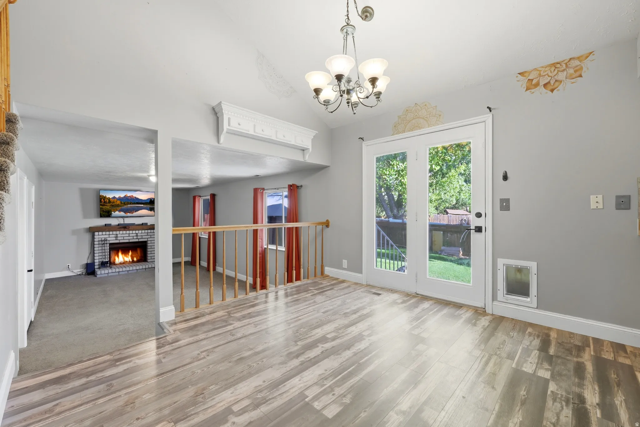 Spacious interior with wood-finish flooring, a contemporary chandelier, and white French doors opening to outdoor green space