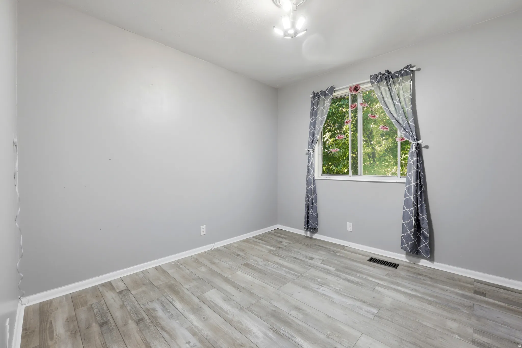 Room featuring light gray walls, wood-finish flooring, and a single window