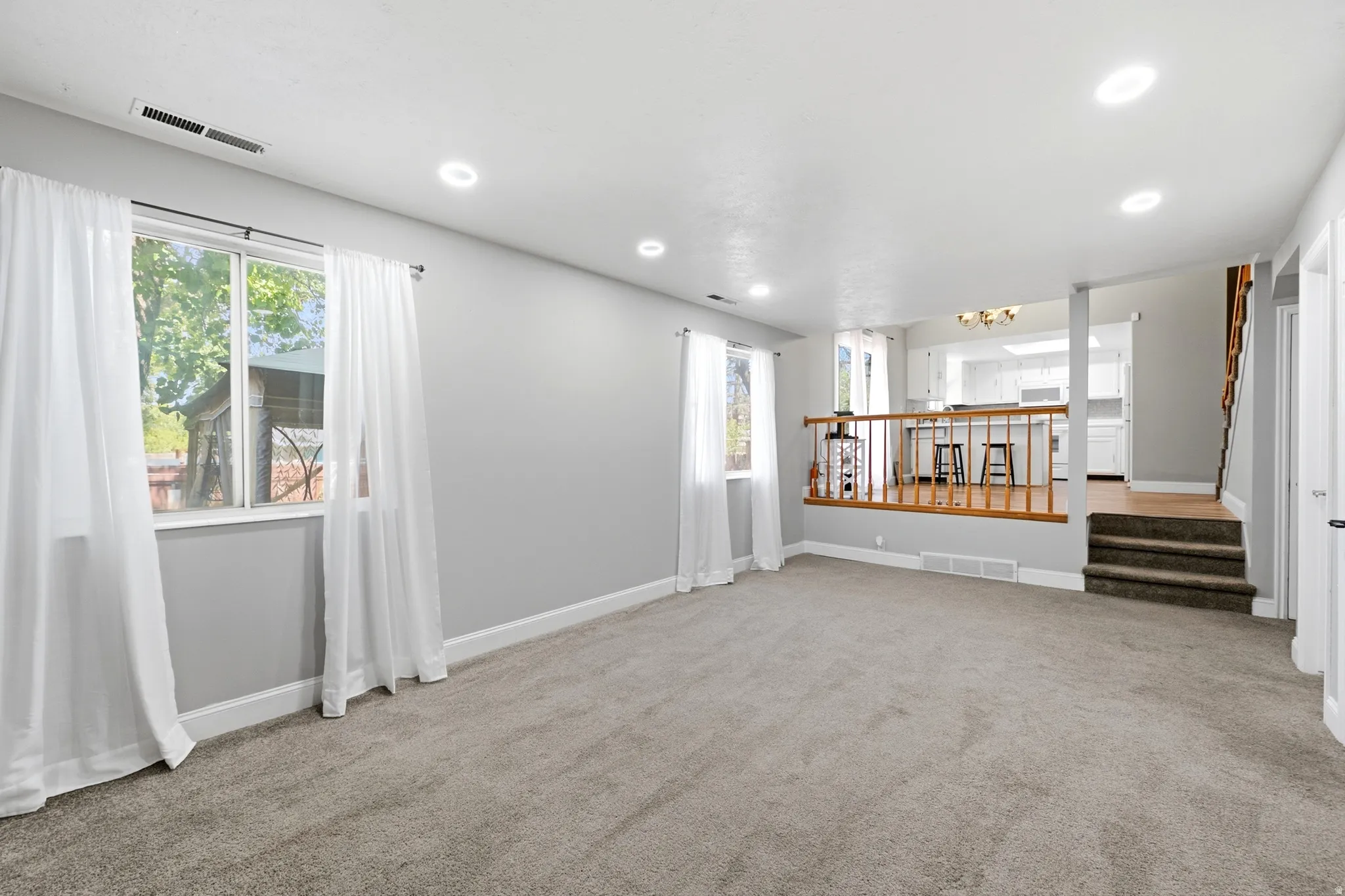 Carpeted living area with recessed lighting, two windows, and light gray walls