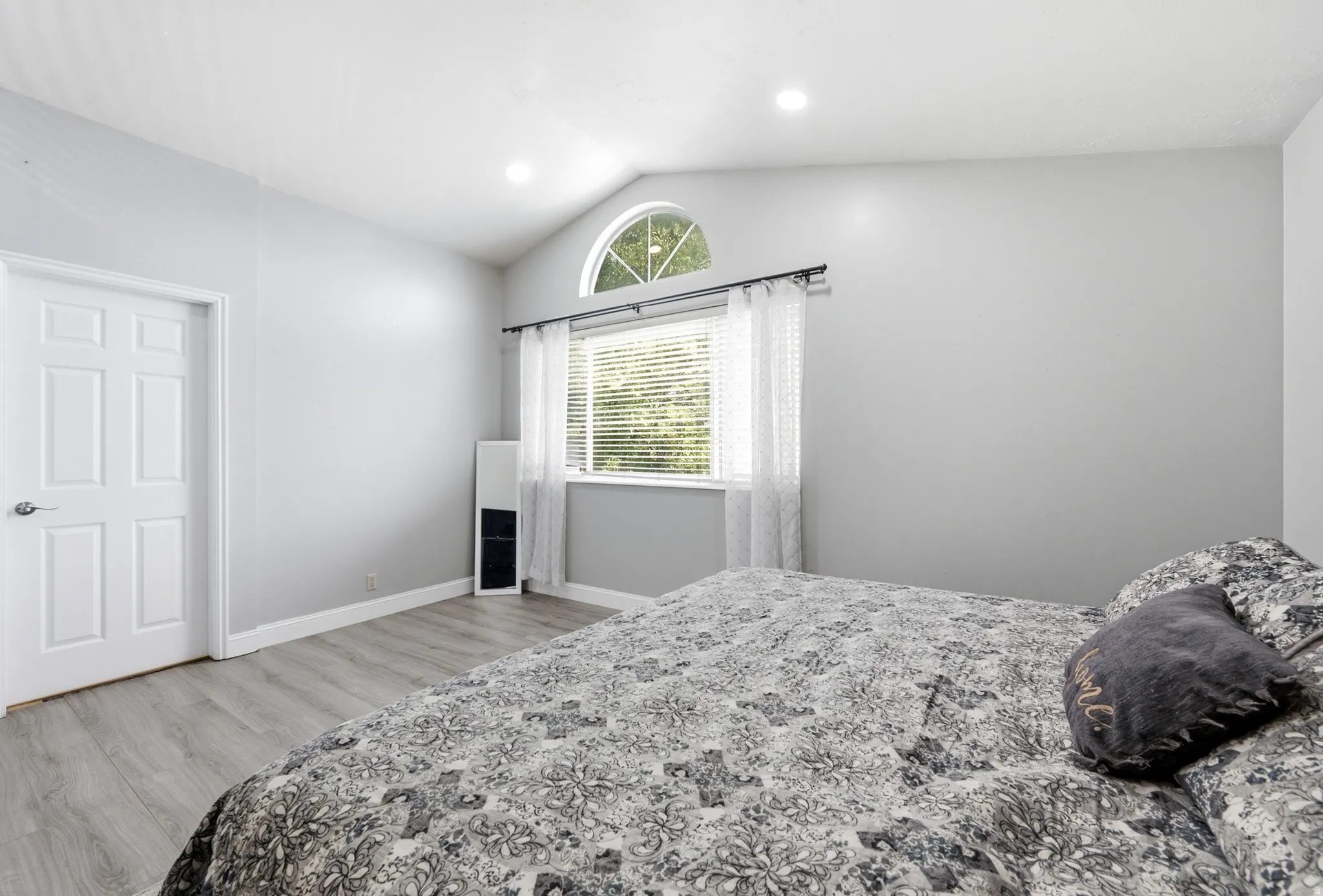 Vaulted ceiling, arched window accent, recessed lighting, wood-finish flooring, and a paneled interior door
