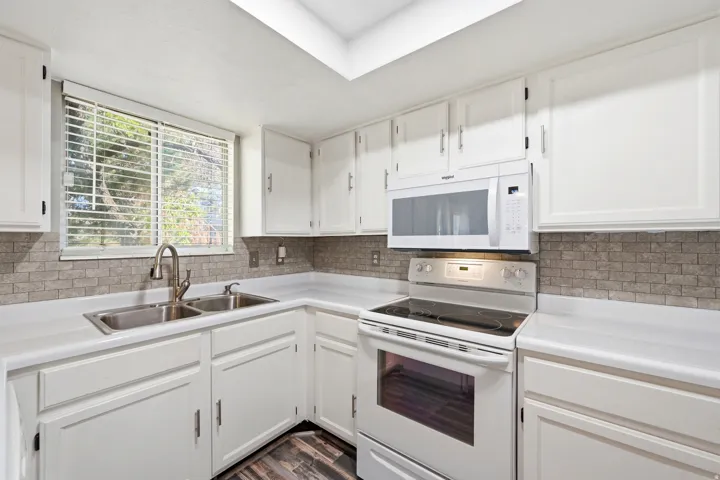 White cabinetry, white countertops, stainless steel double basin sink, white range, and stone tile backsplash