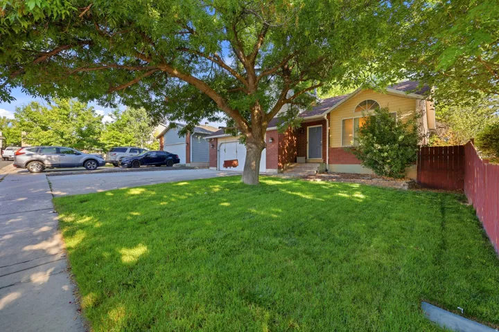 Exterior featuring a mature tree providing shade, a manicured lawn, a detached two-car garage, and a fenced side yard