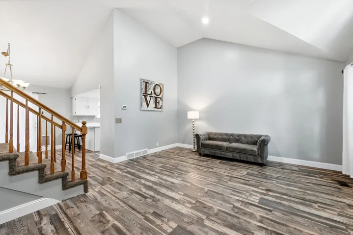 Vaulted ceilings, wood-finish flooring, staircase with wood railing, white baseboards, and neutral wall tones
