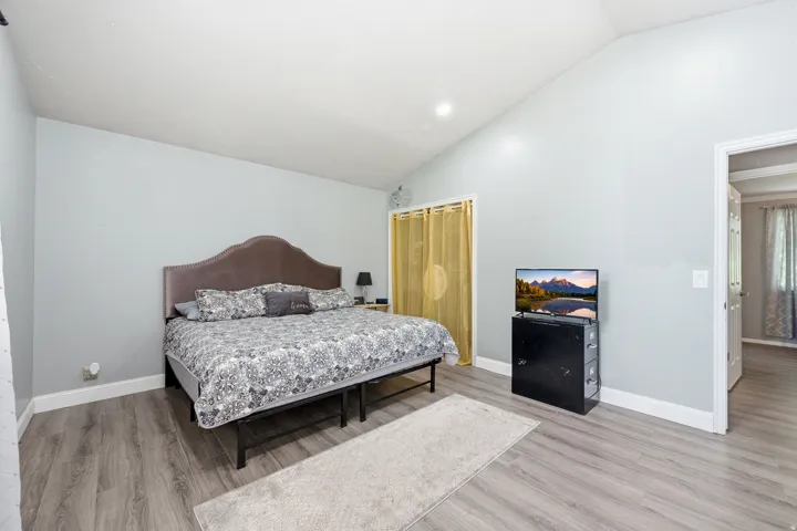 Vaulted ceiling, wood-finish flooring, light gray wall color, recessed lighting, and a closet with a curtain enclosure