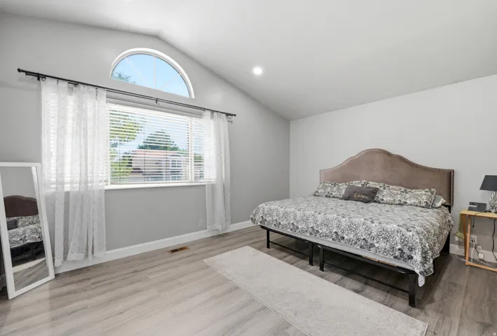 Vaulted ceiling, arched transom window, wood-finish flooring, recessed lighting, and a large window with blinds