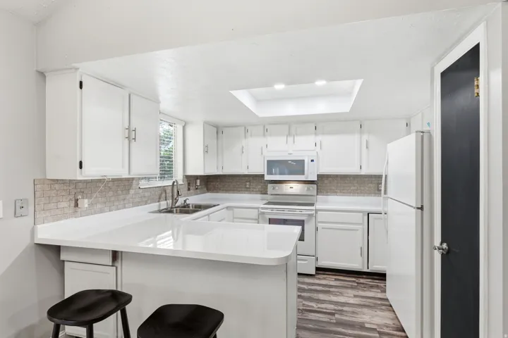 White cabinetry, light-toned countertops, tile backsplash, wood-finish flooring, and a ceiling skylight