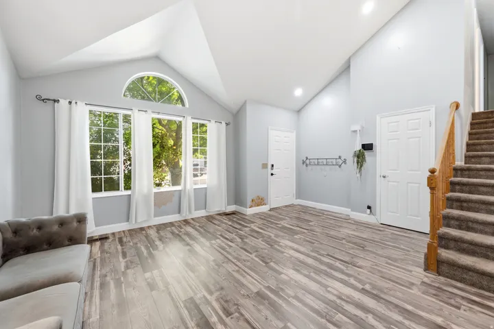 Vaulted ceiling, wood-finish flooring, arched transom window, recessed lighting, and a staircase with wood railing