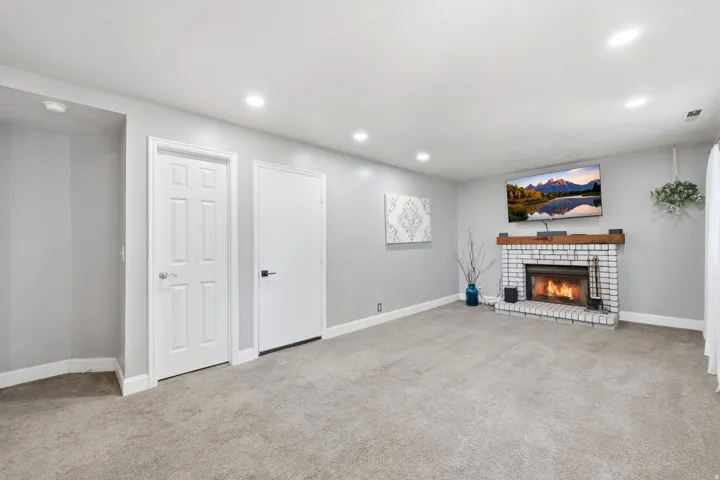 Spacious room featuring a white brick fireplace with a wood mantel, soft gray carpet, recessed lighting, and crisp white trim