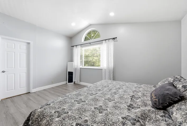 Vaulted ceiling, arched window accent, recessed lighting, wood-finish flooring, and a paneled interior door